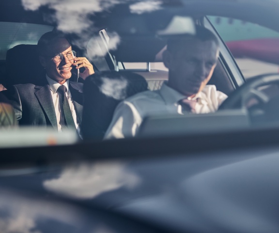 Smiling businessman with smartphone travelling with chauffeur